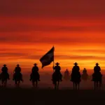 Revolucionarios a caballo bajo un cielo rojo, símbolo de la lucha y pasión de la Revolución Mexicana.